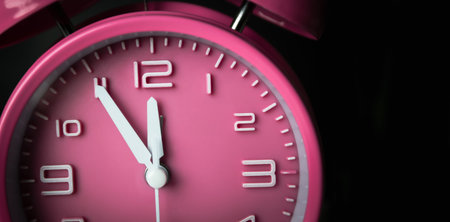 Pink alarm clock setting at five before noon or midnight. A Time conceptual