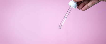 Woman hand drop tube to drop water or serum. A Cosmetic pipette with drops of oilの写真素材