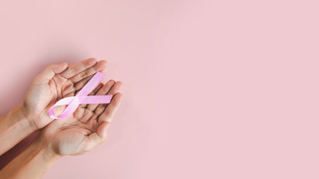 Woman hand is holding pink bow ribbon in hand to encourage breast cancer patient and support a breast cancer campaign in October monthの写真素材
