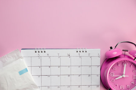 Women's menstruation Calendar, sanitary napkin in a package with pink alarm clock on a pink background.  Concept of critical days time.の写真素材