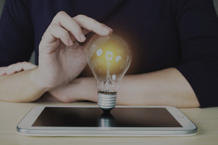 Businesswoman holds glowing lightbulb and is on tablet to input business strategy idea, creative thinking ideas and innovation concept. A Business development and management.の写真素材