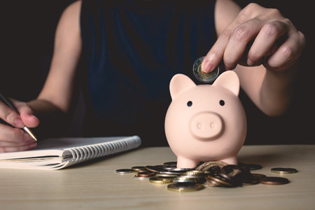 Woman is putting money or coin into piggy bank and writing and note for amount of money and interest rate for saving plan. A Saving money, investment, banking and finance concept.の写真素材