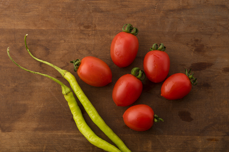 Vegetable: Top View of Fresh Red Baby Tomatoes and Green Chilies on Brown Wooden Backgroundの写真素材