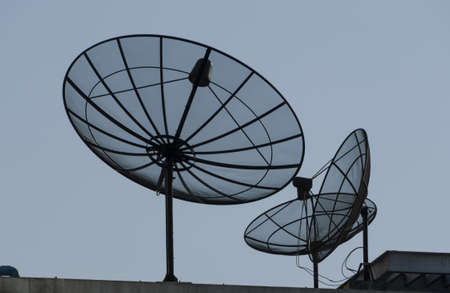 communication satellite dish on top roof over blue skyの写真素材