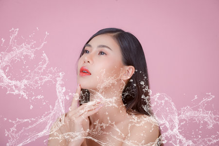 Portrait of a woman using water to wash her face, Beauty Spa Woman with perfect skin Portrait. Asian beautiful woman skin makeup young model,on pink studioの写真素材