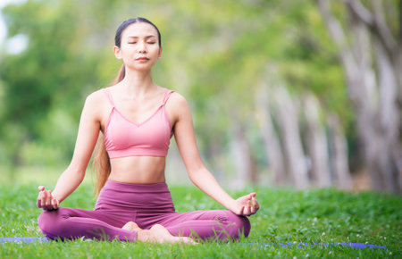 Asian model poses yoga in a park on a natural green background, health care concept, beautiful body structure, fit bodyの写真素材