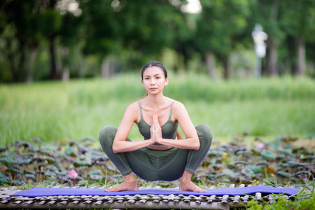 Asian model poses yoga in a park on a natural green background, health care concept, beautiful body structure, fit bodyの写真素材
