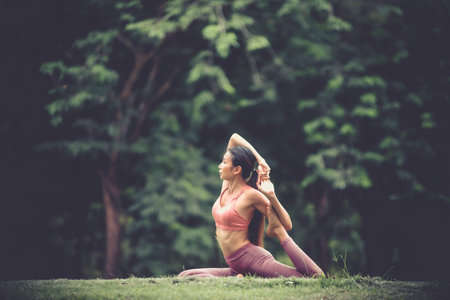 Asian model poses yoga in a park on a natural green background, health care concept, beautiful body...