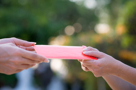 Close up hand sending and receiving red envelope Symbols of the Chinese New Year on golden bokeh background. gifts, festivals and celebration conceptの写真素材