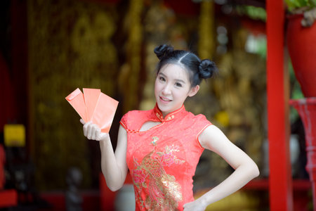 beautiful girl in the Cheongsam red dress up open the red envelope with money, in the Chinese New Year. Festivities, New Year Celebrationのeditorial素材