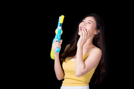 Portrait cheerful young asian woman Wearing a yellow tank top ,holding plastic water gun Smiling and having fun playing in the water Songkran festival, Songkran Thailand. isolated on black background.の写真素材