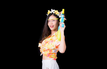 Portrait cheerful young asian woman Wearing a yellow tank top ,holding plastic water gun Smiling and having fun playing in the water Songkran festival, Songkran Thailand. isolated on black background.の写真素材
