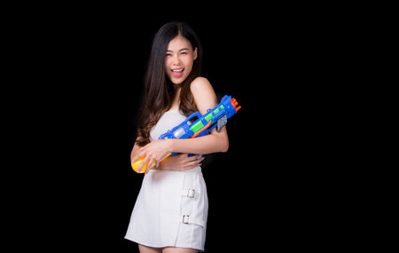 Portrait cheerful young asian woman Wearing a yellow tank top ,holding plastic water gun Smiling and having fun playing in the water Songkran festival, Songkran Thailand. isolated on black background.の写真素材