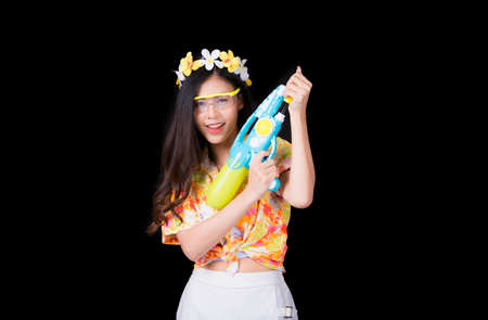 Portrait cheerful young asian woman Wearing a yellow tank top ,holding plastic water gun Smiling and having fun playing in the water Songkran festival, Songkran Thailand. isolated on black background.の写真素材