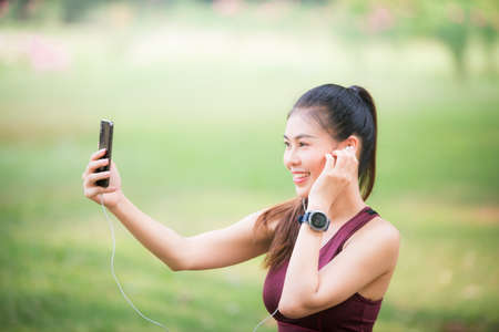 Asian female athletes smile and listen to music on a smartphone Relaxing in the parkの写真素材