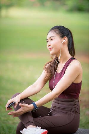 Asian female athletes smile and listen to music on a smartphone Relaxing in the parkの写真素材