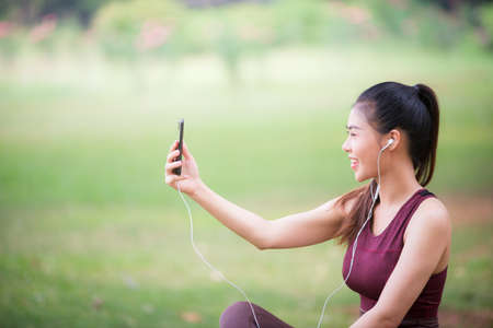 Asian female athletes smile and listen to music on a smartphone Relaxing in the parkの写真素材