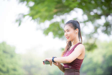 Asian female athletes smile and listen to music on a smartphone Relaxing in the parkの写真素材