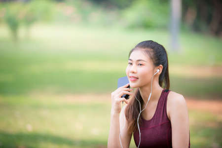 Asian female athletes smile and listen to music on a smartphone Relaxing in the parkの写真素材