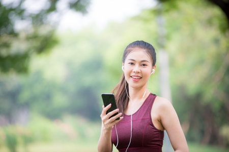 Asian female athletes smile and listen to music on a smartphone Relaxing in the parkの写真素材
