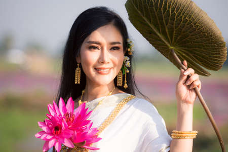 Beautiful girl in White Thai dress with red lotus flowers.Thai girl in retro Thai dress,Beautiful Thai girl in traditional dress costumeの写真素材