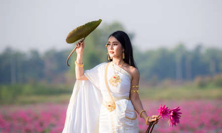 Beautiful girl in White Thai dress Sitting on a wooden boat in the red lotus pond.Thai girl in retro Thai dress,Beautiful Thai girl in traditional dress costumeの写真素材
