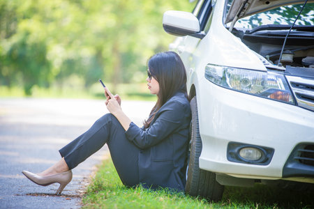 Asian businesswoman is stressed because the car is stuck and standing next to the car is waiting for...