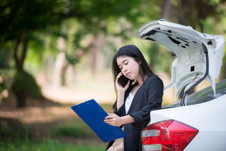 Asian businesswoman is stressed because the car is stuck and standing next to the car is waiting for the mechanic.の写真素材