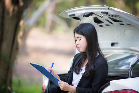 Asian businesswoman is stressed because the car is stuck and standing next to the car is waiting for the mechanic.の写真素材