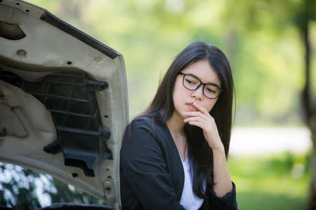 Asian business woman sad waiting for help by a broken car. Use a mobile phone to call the mechanic.の写真素材