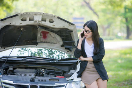 Asian businesswoman is stressed because the car is stuck and standing next to the car is waiting for the mechanic.の写真素材