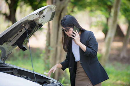 Asian business woman sad waiting for help by a broken car. Use a mobile phone to call the mechanic.の写真素材