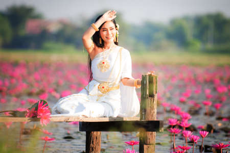 Beautiful girl in White Thai dress with red lotus flowers.Thai girl in retro Thai dress,Beautiful Thai girl in traditional dress costumeの写真素材