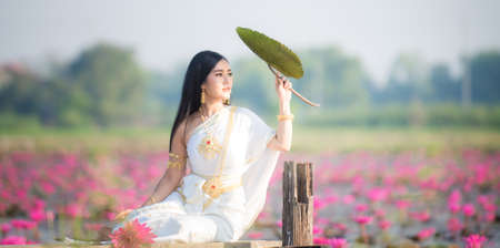 Beautiful girl in White Thai dress with red lotus flowers.Thai girl in retro Thai dress,Beautiful Thai girl in traditional dress costumeの写真素材
