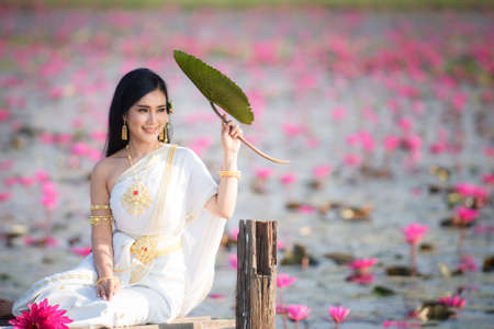 Beautiful girl in White Thai dress with red lotus flowers.Thai girl in retro Thai dress,Beautiful Thai girl in traditional dress costumeの写真素材