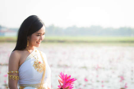 Beautiful girl in White Thai dress with red lotus flowers.Thai girl in retro Thai dress,Beautiful Thai girl in traditional dress costumeの写真素材