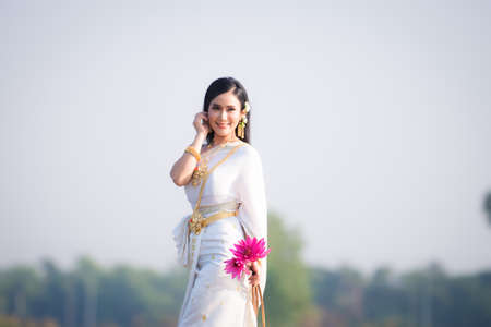 Beautiful girl in White Thai dress with red lotus flowers.Thai girl in retro Thai dress,Beautiful Thai girl in traditional dress costumeの写真素材