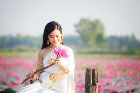 Beautiful girl in White Thai dress with red lotus flowers.Thai girl in retro Thai dress,Beautiful Thai girl in traditional dress costumeの写真素材