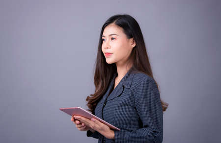 Portrait of Asian woman, happy working day.beautiful modern businesswoman ,holding tablet computer on Gray background in the studioの写真素材