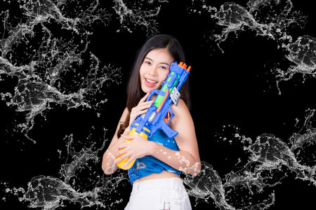 Portrait cheerful young asian woman Wearing a yellow tank top ,holding plastic water gun Smiling and having fun playing in the water Songkran festival, Songkran Thailand. isolated on black background.の写真素材