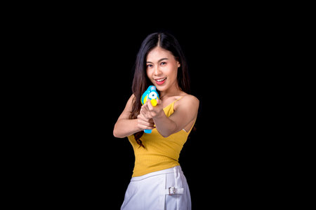 Portrait cheerful young asian woman Wearing a yellow tank top ,holding plastic water gun Smiling and having fun playing in the water Songkran festival, Songkran Thailand. isolated on black background.の写真素材