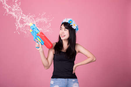 Portrait cheerful young asian woman holding plastic water gun Smiling and having fun playing in the water Songkran festival, Thailand. isolated on pink background. Thai New Year's Day.の写真素材