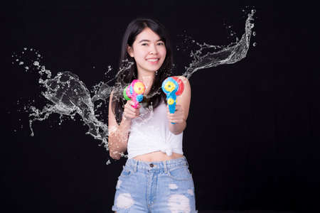 Portrait cheerful young asian woman Wearing a red tank top ,holding plastic water gun Smiling and having fun playing in the water Songkran festival, Songkran Thailand. isolated on black background.の写真素材
