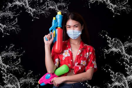 Portrait cheerful young asian woman holding plastic water gun Smiling and having fun playing in the water Songkran festival, Thailand. isolated on black background. Thai New Year's Day.の写真素材