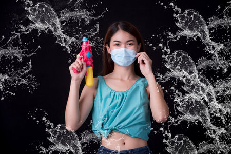 Portrait cheerful young asian woman holding plastic water gun Smiling and having fun playing in the water Songkran festival, Thailand. isolated on black background. Thai New Year's Day.の写真素材