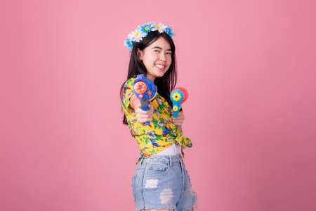 Portrait cheerful young asian woman holding plastic water gun Smiling and having fun playing in the water Songkran festival, Thailand. isolated on pink background. Thai New Year's Day.の写真素材