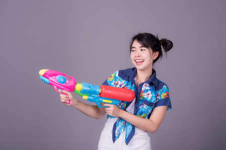 Portrait cheerful young asian woman Wearing a yellow tank top ,holding plastic water gun Smiling and having fun playing in the water Songkran festival, Songkran Thailand. isolated on black background.の写真素材