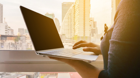 business woman Standing by the window with views of the city and Using laptop Then look at the Sun light .の写真素材