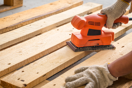 Wood sanding machines , Carpenter working with electrical sander on pine floor or table surfaceの写真素材
