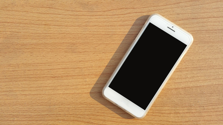 Modern mobile smart phone with black screen for mockup On a wooden table .の写真素材